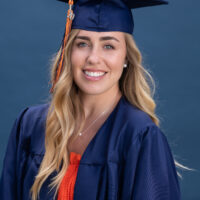 Natural light portrait of a young woman in graduation cap and gown on a blue background