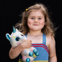 Natural light portrait of a little girl with a stuffed unicorn on black background